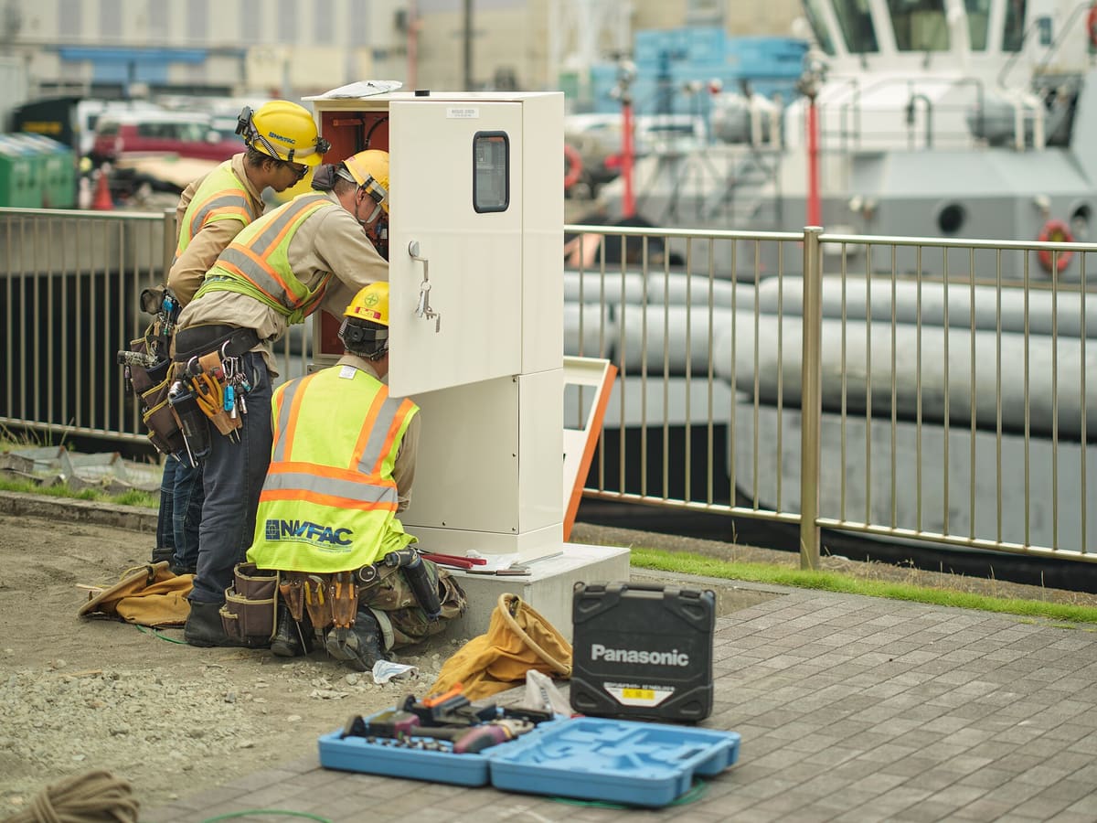 Technicians in safety vests wiring the base cabinet of an outdoor LED sign